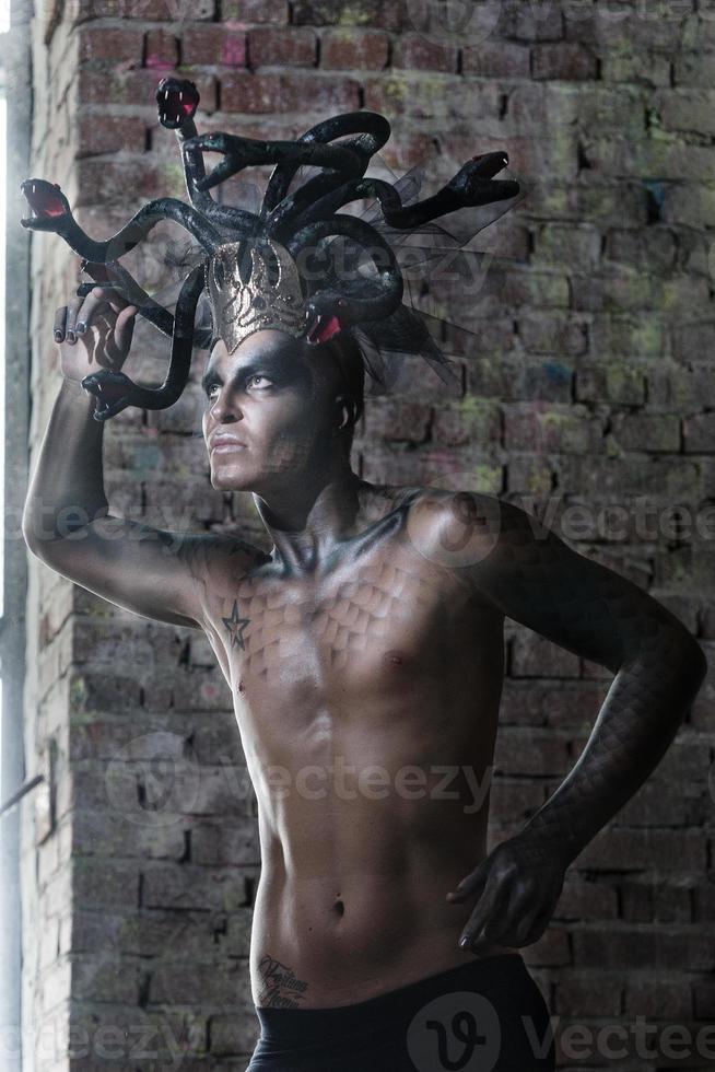 portrait of a man in the image of a basilisk with body art with a naked torso and a headdress in the form of a bunch of snakes photo
