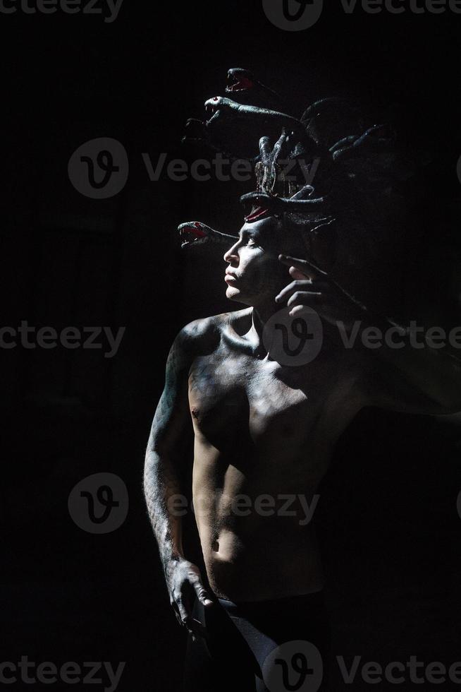 portrait of a man in the image of a basilisk with body art with a naked torso and a headdress in the form of a bunch of snakes photo