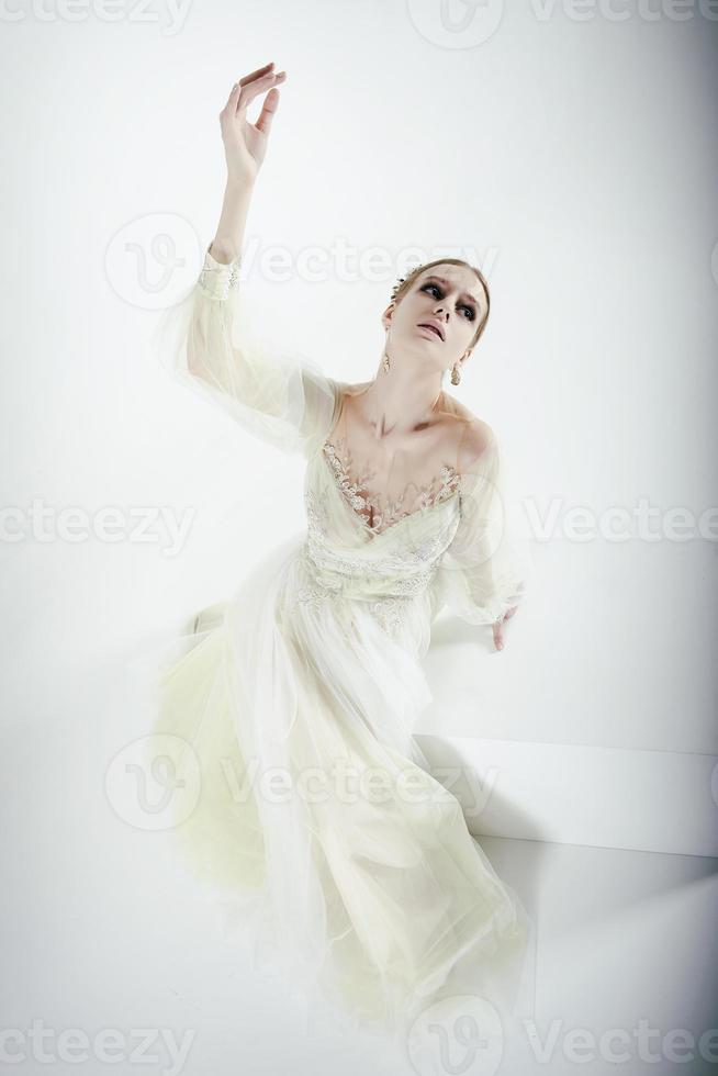 young girl model in a photo studio in a wedding dress gestures with her hands posing from a top angle