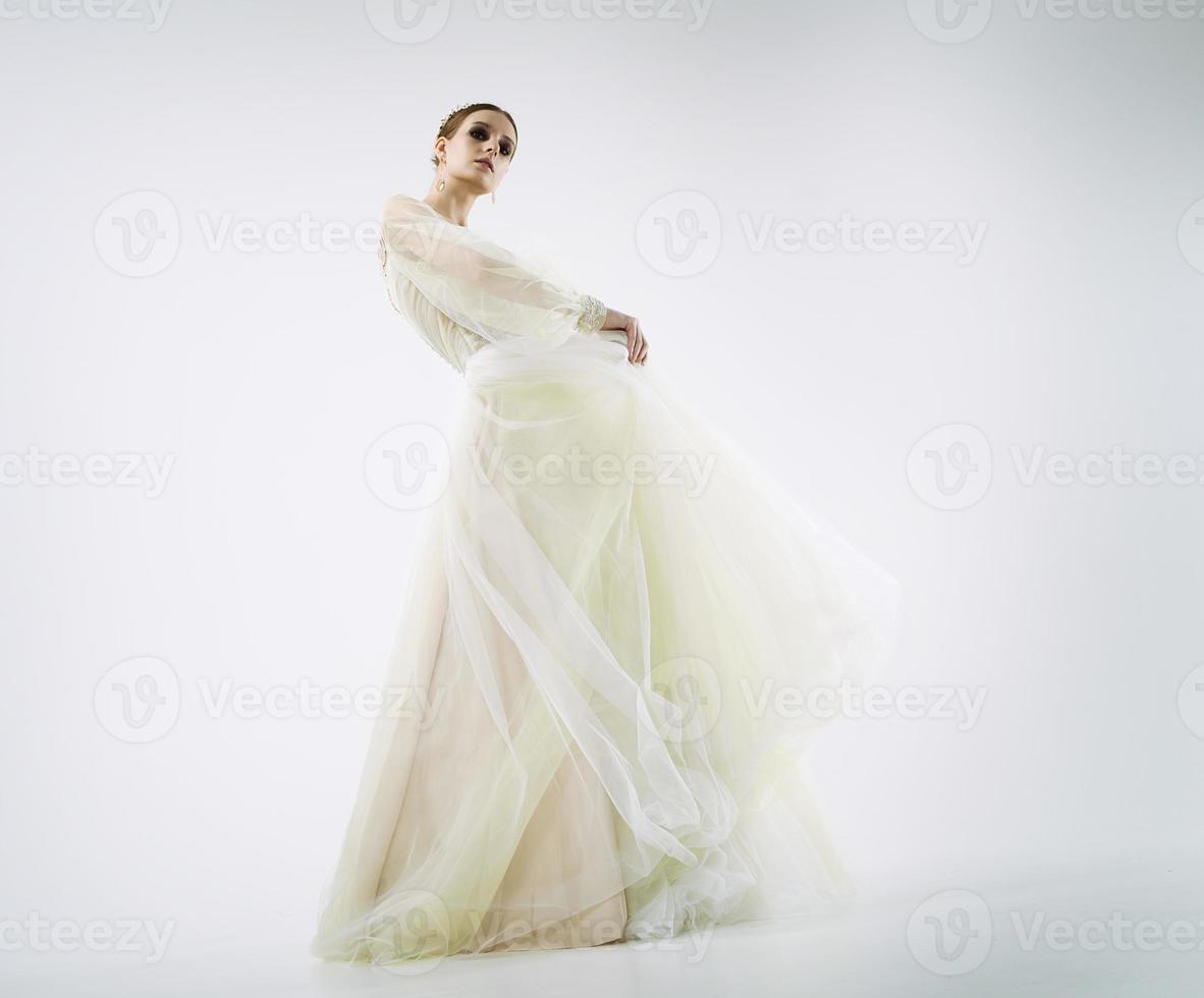 young girl model in a photo studio in a wedding dress poses dynamically raising her legs and arms