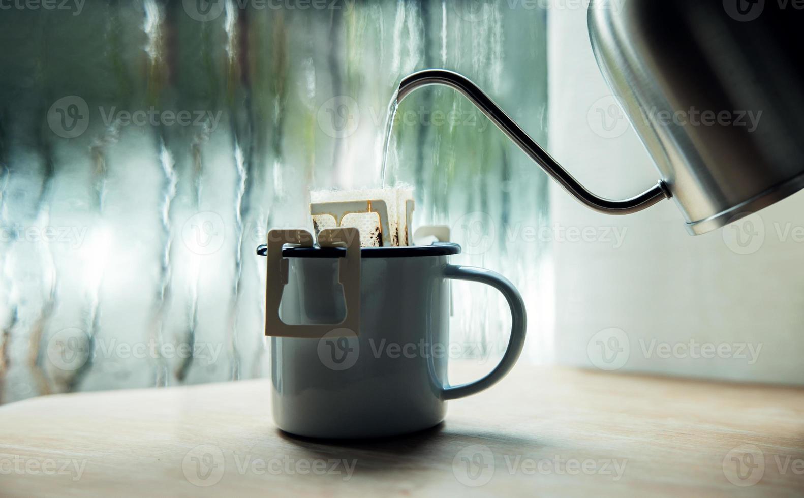 Dripping Coffee by the Window on Morning Rainy Day. Making Hot Drink by Pouring Hot Water from kettle into an Instant Coffee Drip Bag. Relaxing, Enjoying with Harmony Living Lifestyle photo