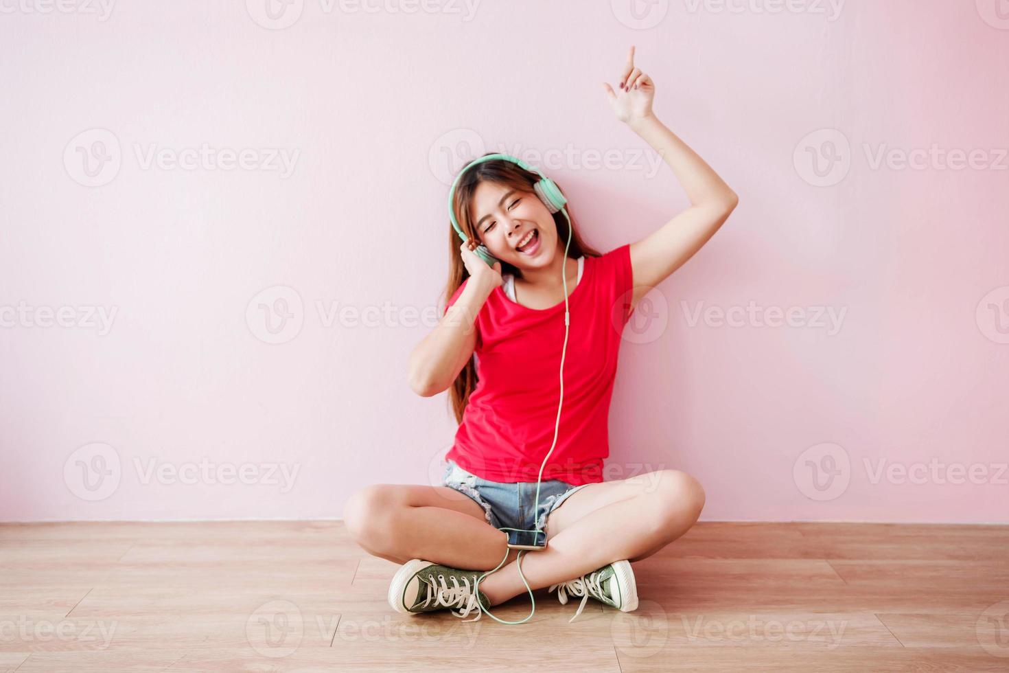 enfoque suave de una joven feliz escuchando música desde un teléfono móvil en casa, sentada en el suelo, con los ojos cerrados y sonriendo foto