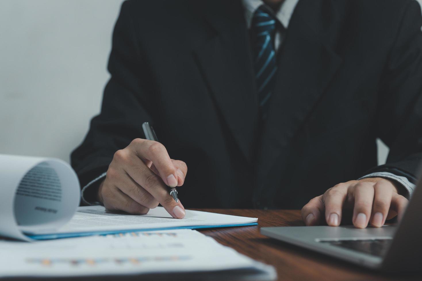 Businessman holding pen document graph accounting finance paper work analysis chart marketing investment and report economy with computer laptop on desk at office. photo
