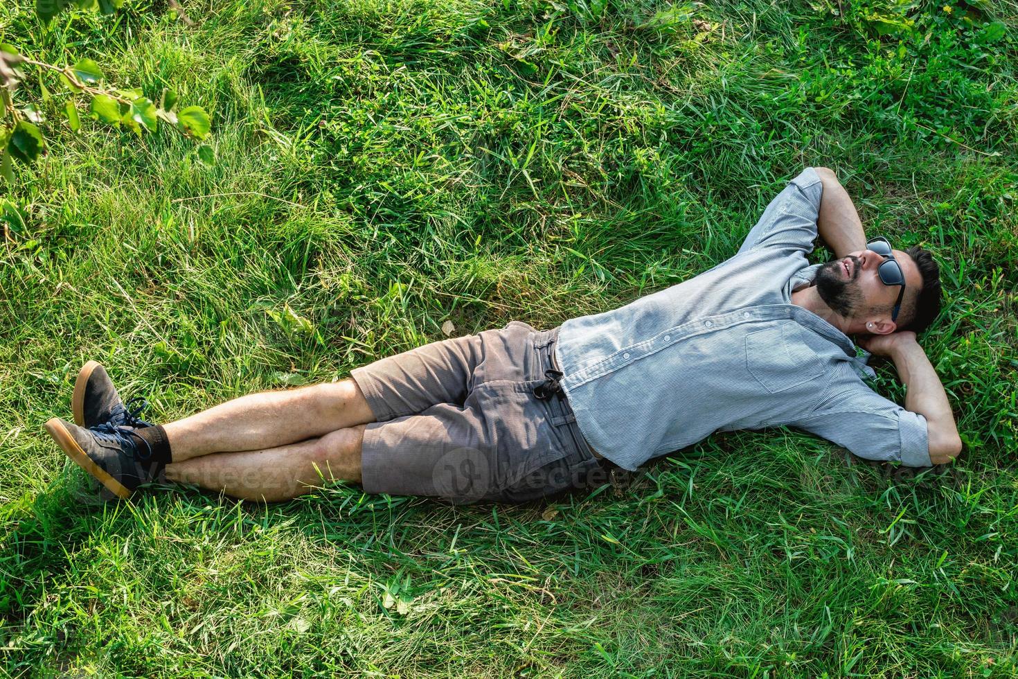 Young handsome sports European man in sunglasses is resting on a grass in summer park, top view. photo