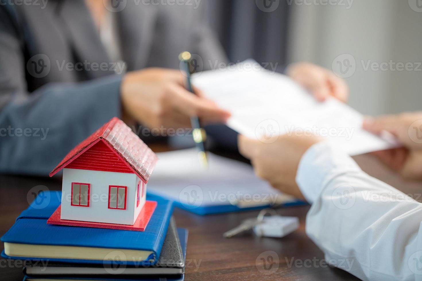 Woman home sales person is checking documents for house purchase contract before letting the customer sign contract on table is key with house model, real estate trading and insurance property concept photo