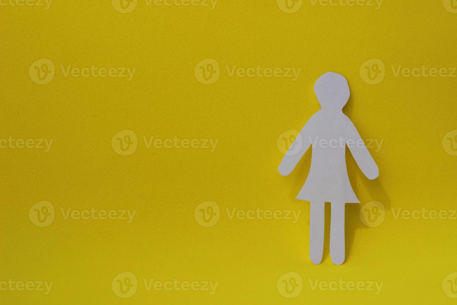 Silhouette of a woman in dress of white paper, cut by hand. On right side of photo with copy space on yellow background.