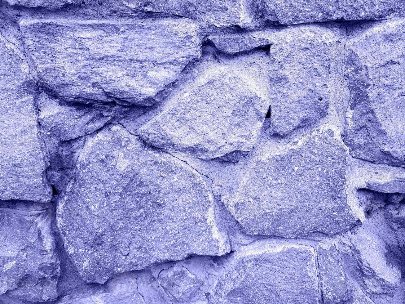 Old stone wall repainted in trendy very peri color of the year 2022. Rough texture. Violet stone background with place for text. photo