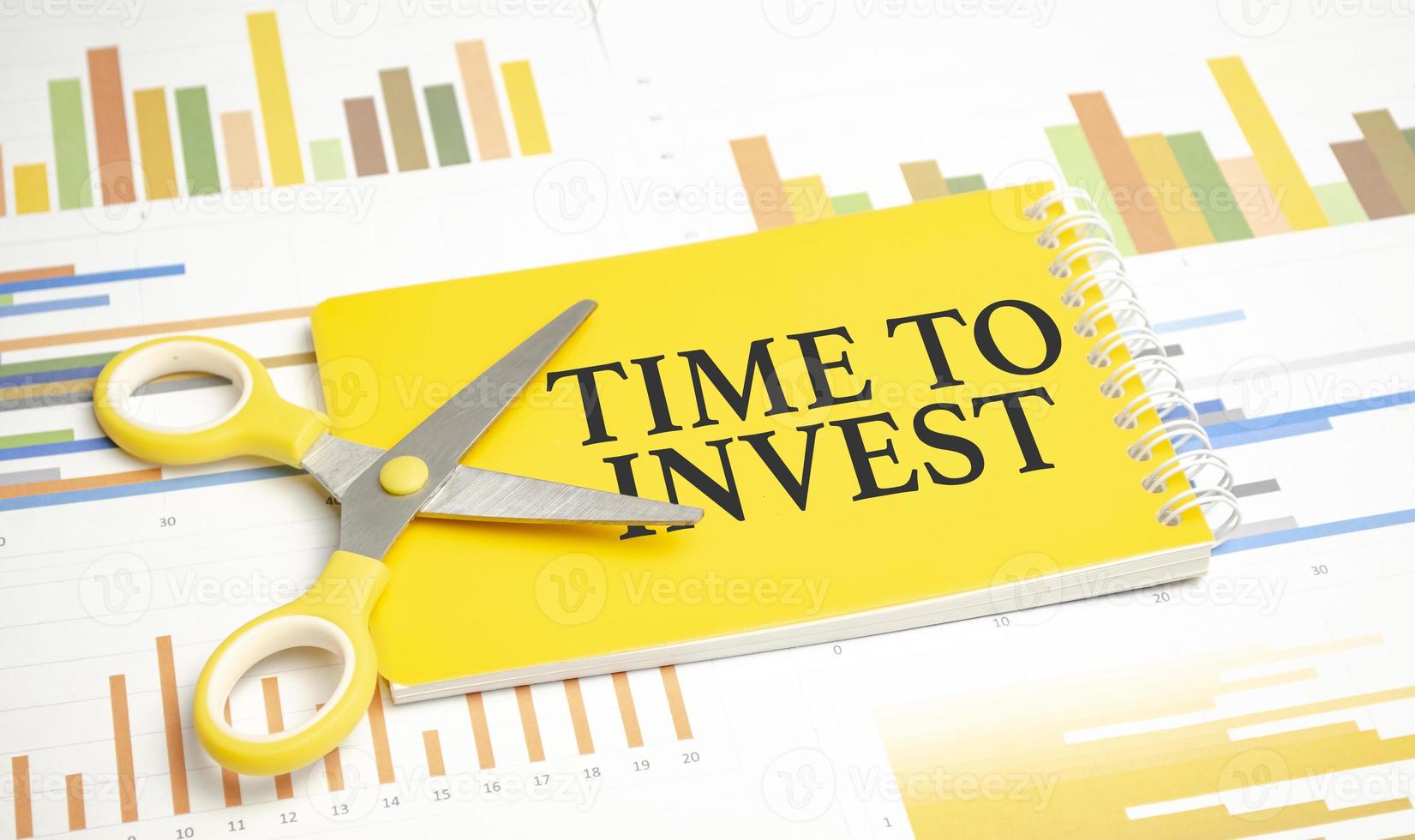 TIME TO INVEST text on a yellow sticky on clipboard with chart, wooden background photo