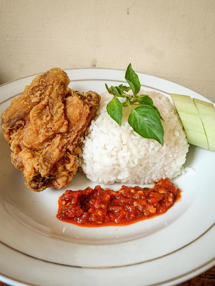 White rice served on a white plate with side dishes of fried chicken, sambal and cucumber photo