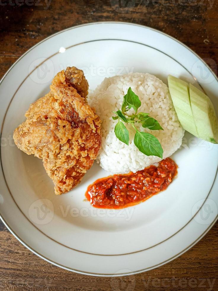 White rice served on a white plate with side dishes of fried chicken, sambal and cucumber photo