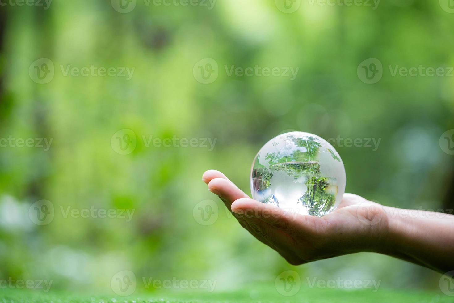 Human hand holding globe planet glass In green forest with bokeh nature lights. world environment day. concept for environment conservation, protect ecology earth and environmental eco-friendly life. photo