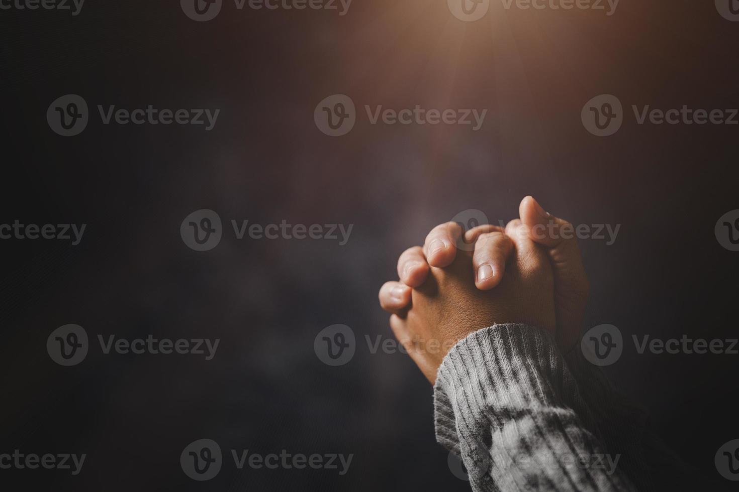 mano de persona de oración en fondo negro. la mujer católica cristiana está rezando a dios en la oscuridad en la iglesia. chica cree y fe en jesucristo. la religión de cristo y el cristianismo adoran o rezan concepto. foto