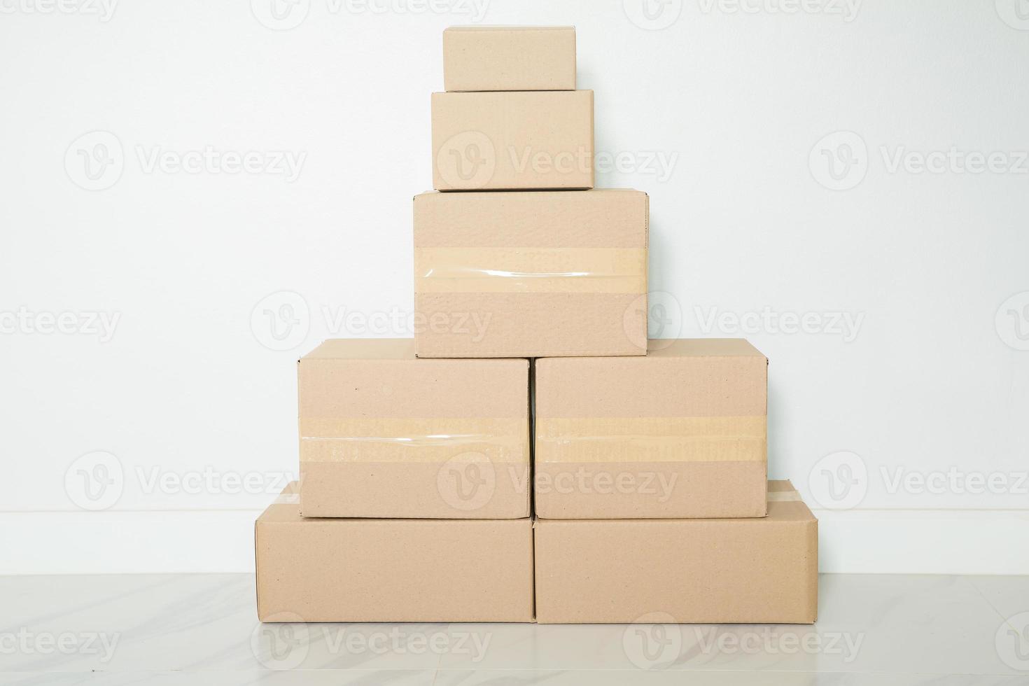 pila de cajas de cartón para mudanzas, habitación vacía con una pared blanca y cajas de cartón con código de barras sin marca en el suelo. entrega de mercancías, compras. cajas de cartón sobre fondo de pared gris. foto