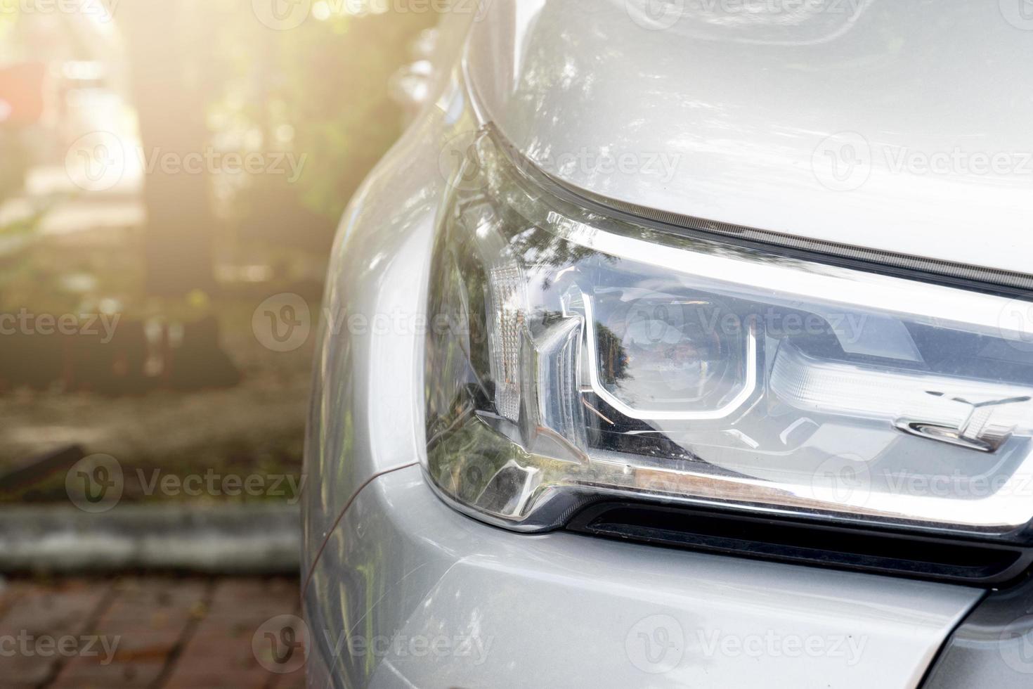 Front headlight of the car parked in the park. Blurred of trees in park area. photo