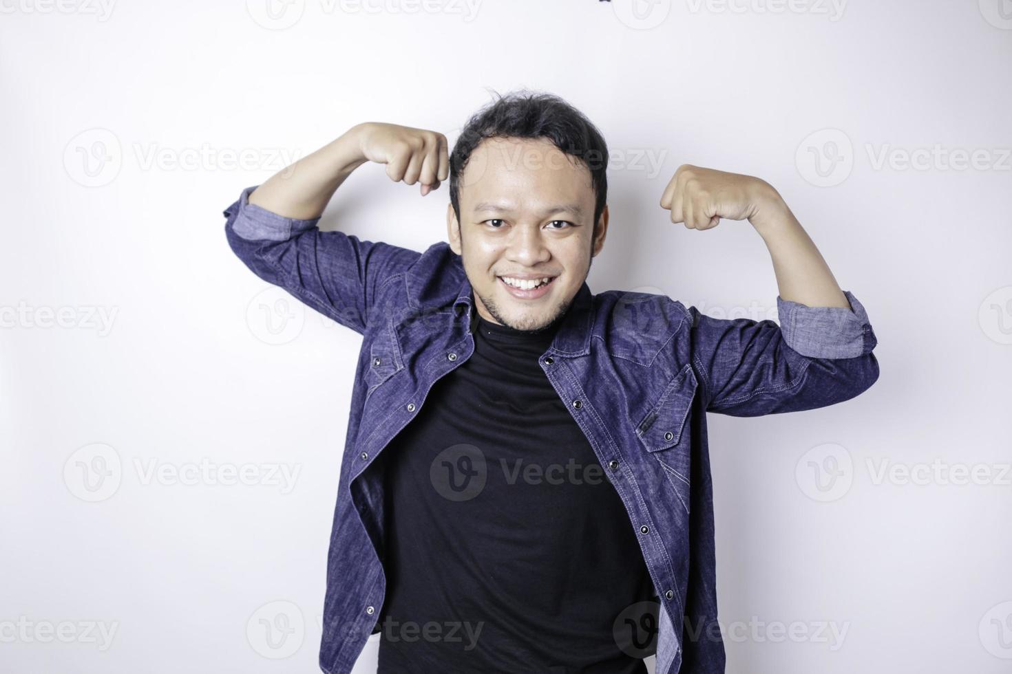 Excited Asian man wearing a navy blue shirt showing strong gesture by lifting his arms and muscles smiling proudly photo