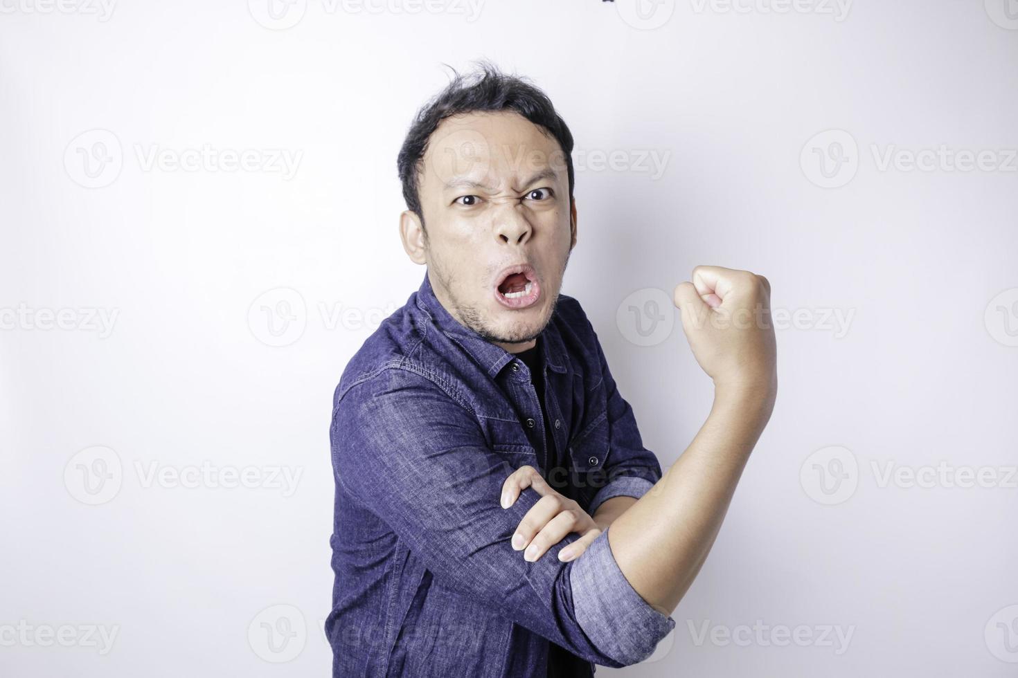 Excited Asian man wearing a navy blue shirt showing strong gesture by lifting his arms and muscles smiling proudly photo