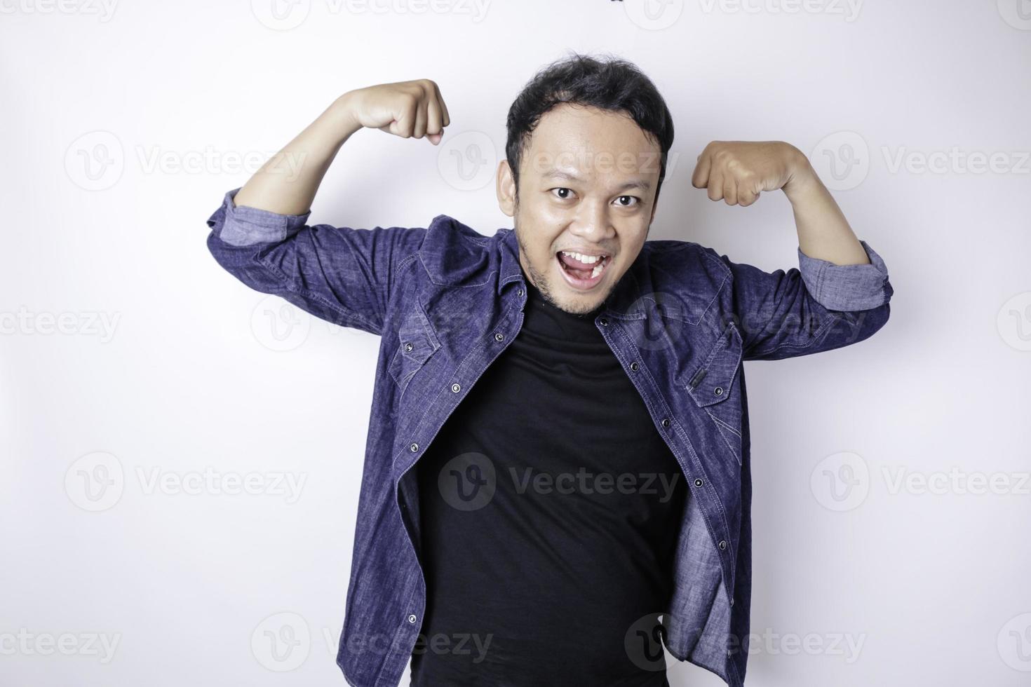 Excited Asian man wearing a navy blue shirt showing strong gesture by lifting his arms and muscles smiling proudly photo