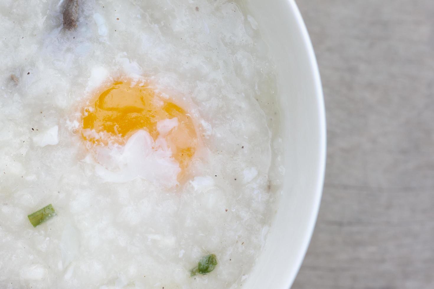 Closeup rice porridge or congee with egg in white bowl on vintage wooden table background. photo