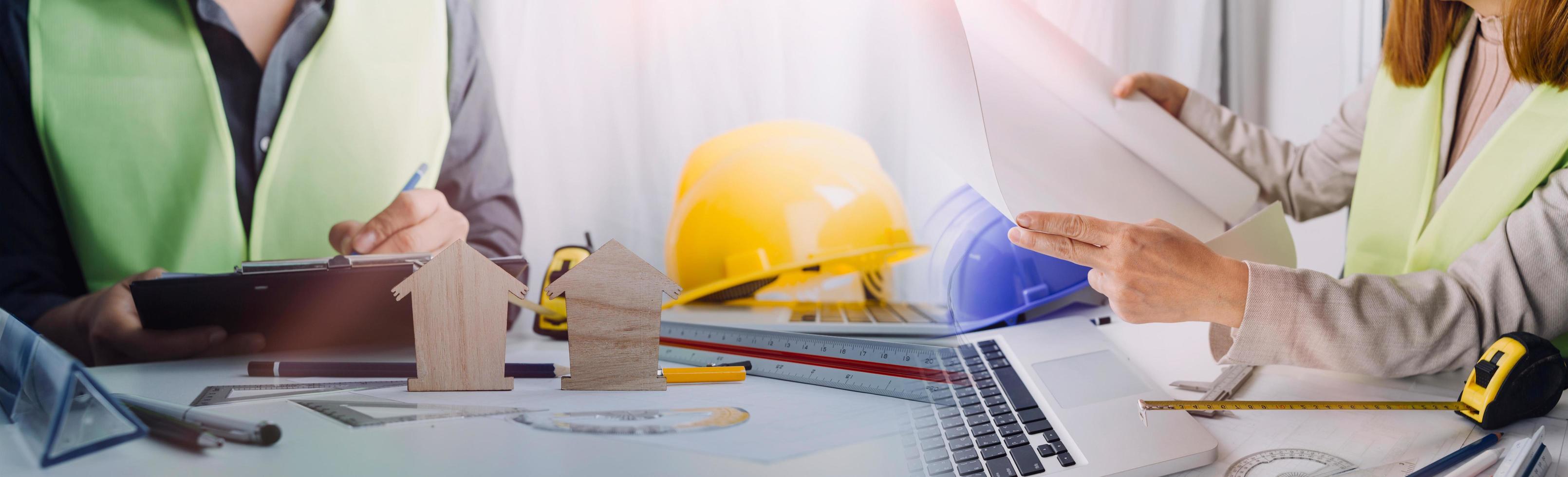 Two colleagues discussing data working and tablet, laptop with on on architectural project at construction site at desk in office photo