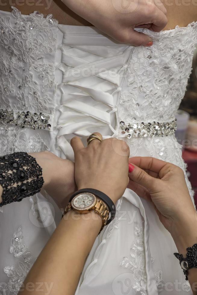 las damas de honor que preparan a una novia para el día de la boda ayudan a sujetar un vestido de novia a la novia antes de la ceremonia. primer plano, concepto de boda. foto