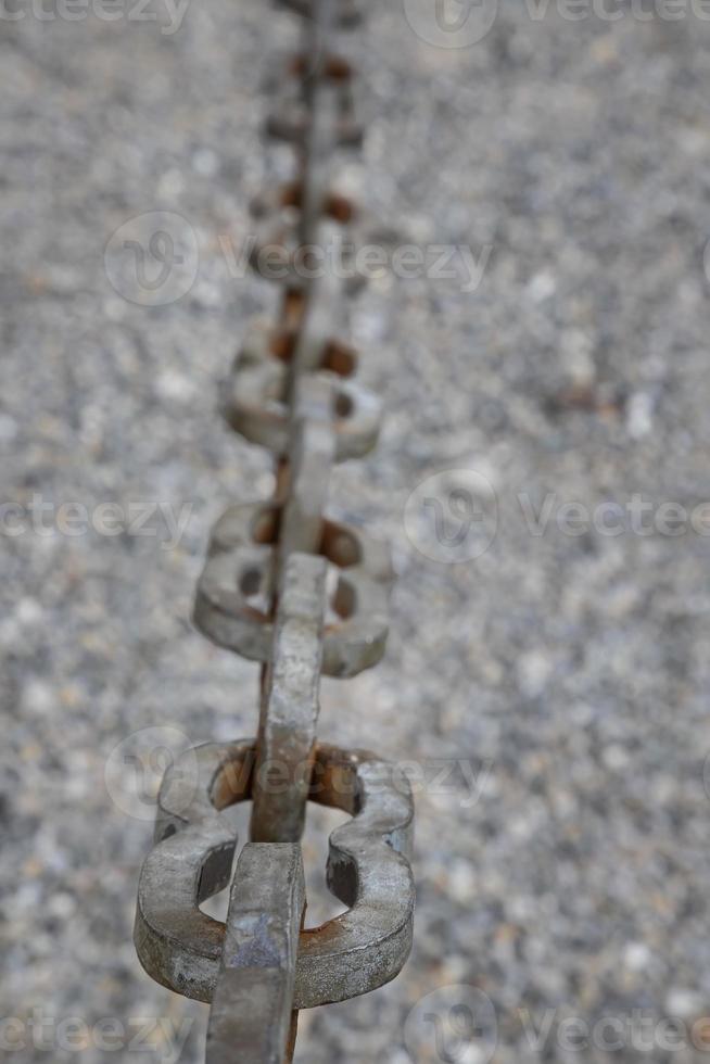 A light gray metal chain made of steel and showing its age is seen up close as it hangs above the broken stone ballast. Selective focus.Vertical view photo