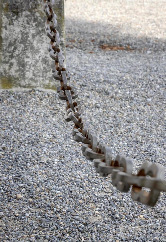 A light gray metal chain made of steel and showing its age is seen up close as it hangs above the broken stone ballast. Selective focus. photo