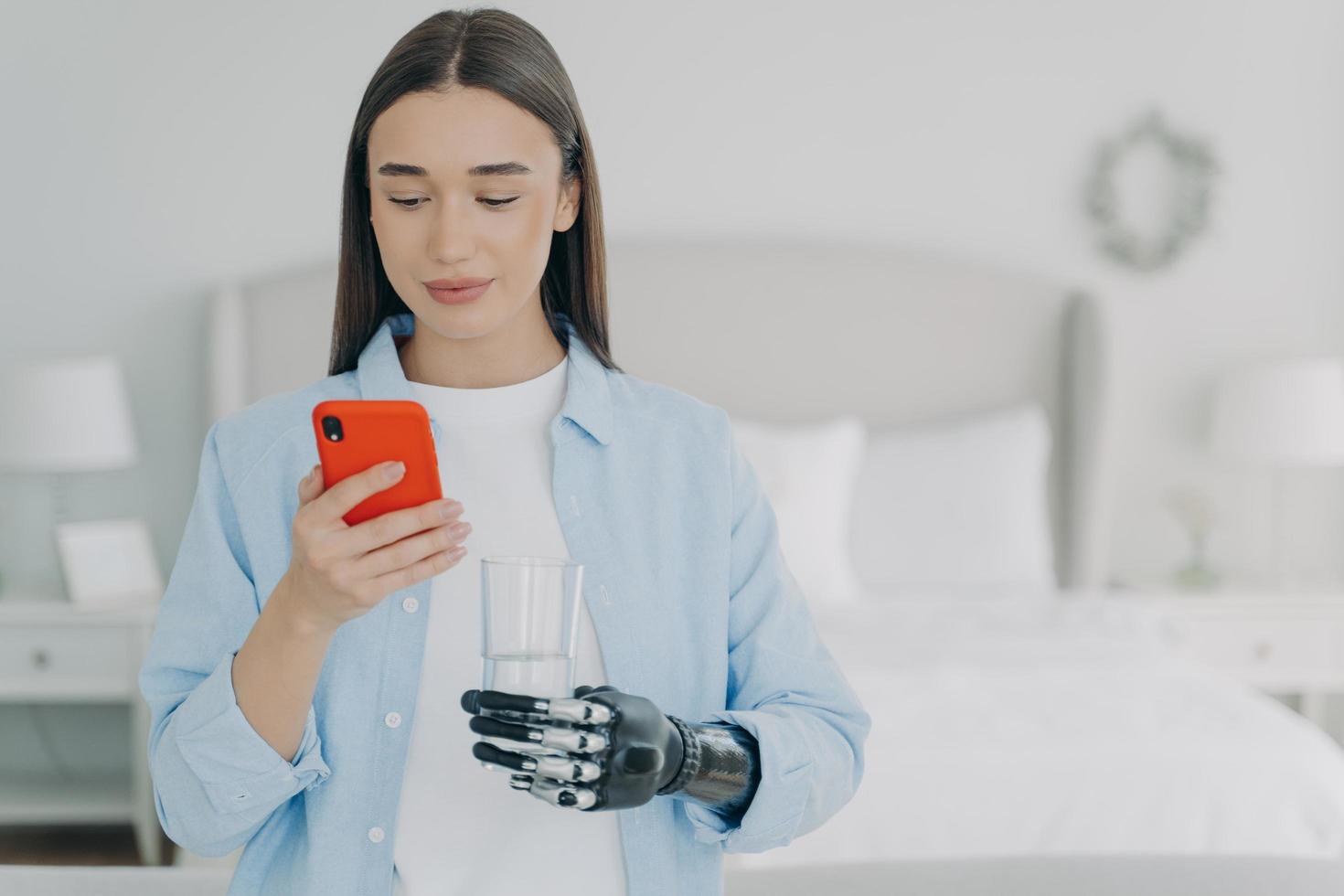 Young disabled girl holds smartphone and glass of water in hands using high tech bionic prosthesis photo