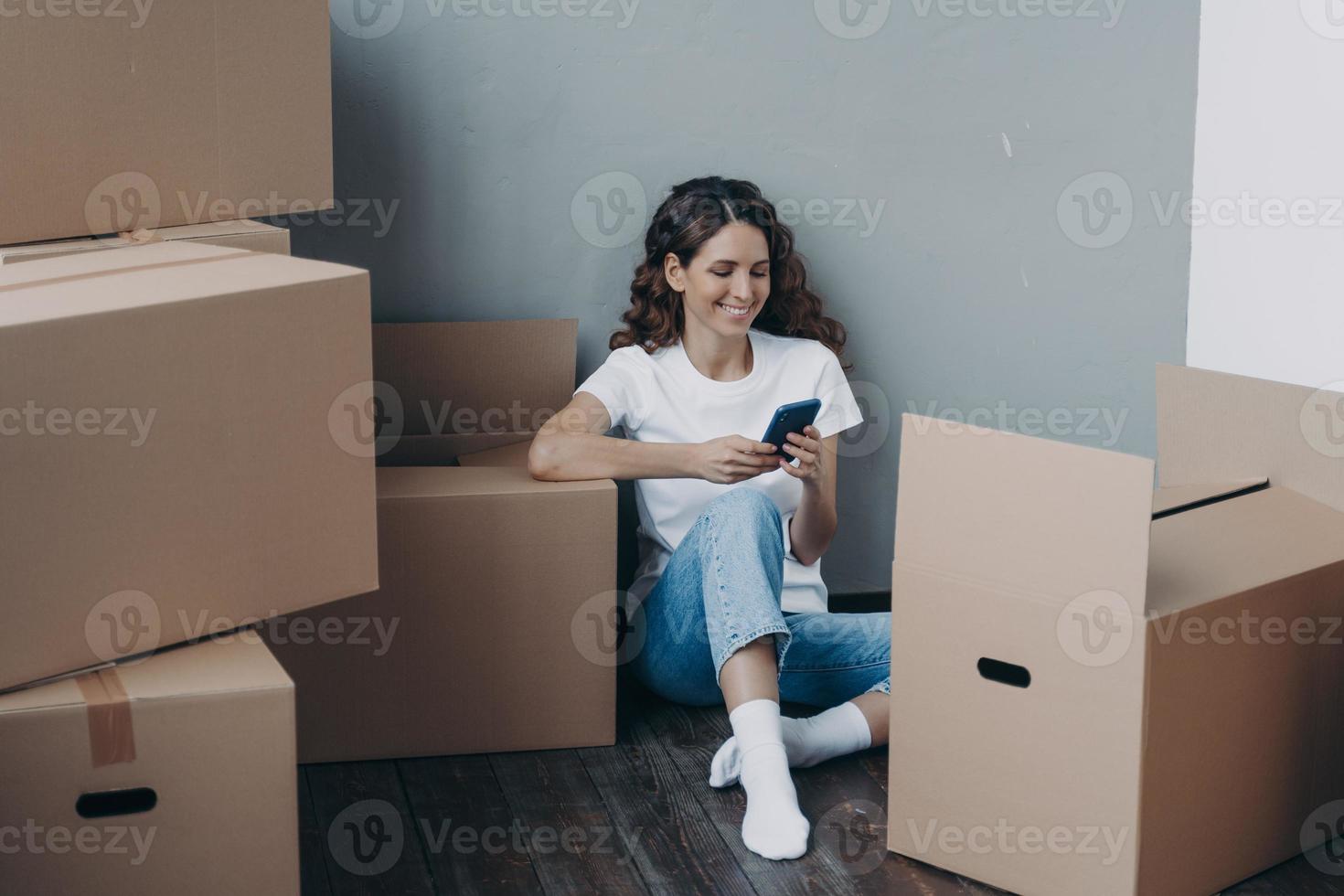 Happy girl uses phone apps, choosing relocation service, answers her mover online. Easy moving day photo