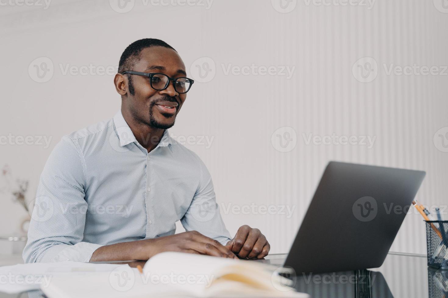 Smiling african american man working on laptop on business project, reading email with good news photo