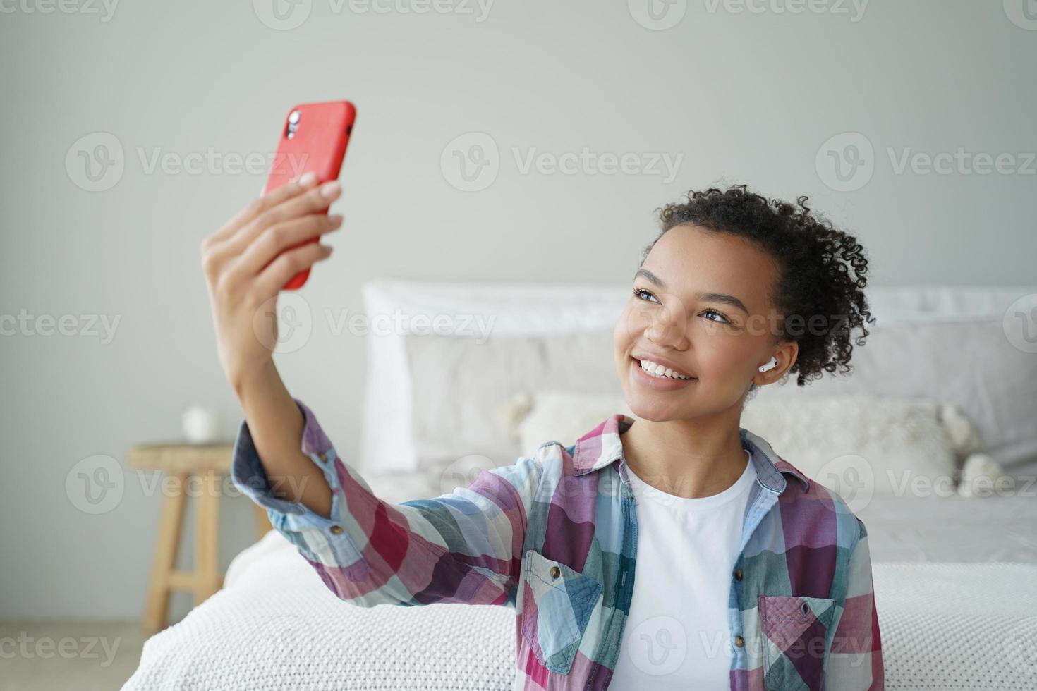 Mixed race teen girl blogger chatting online by phone video call, using modern mobile apps at home photo