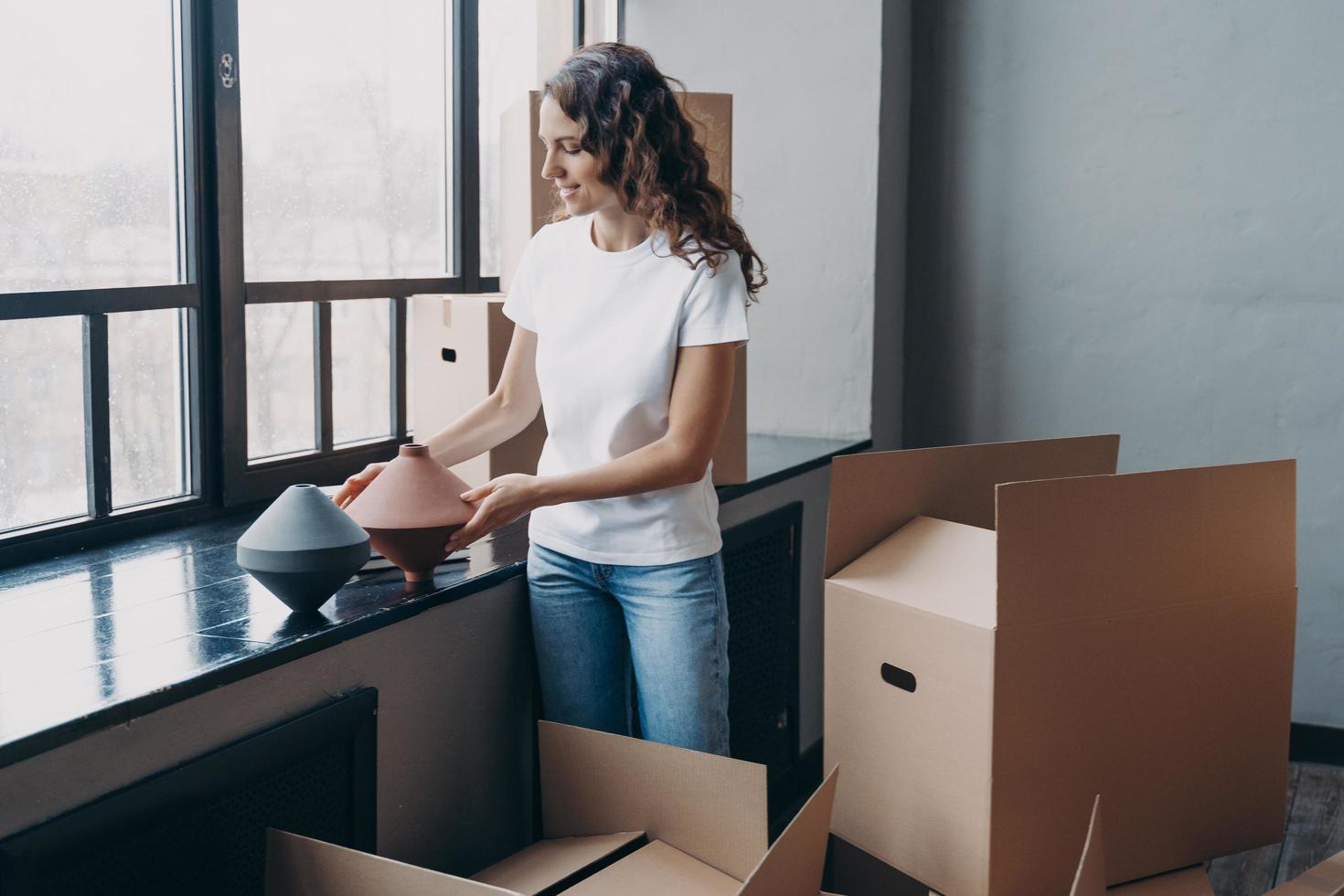 Happy girl unpacks carton box with things at new home on moving day. Transport service advertising photo