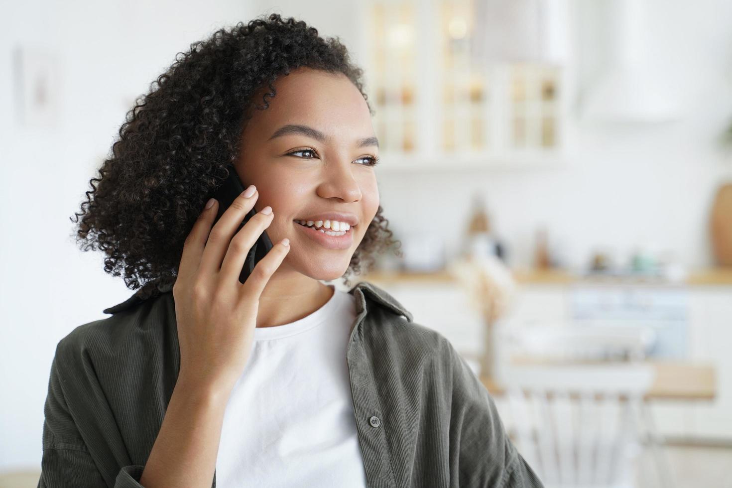 Happy mixed race girl answers call, talking on phone, enjoy pleasant mobile conversation at home photo