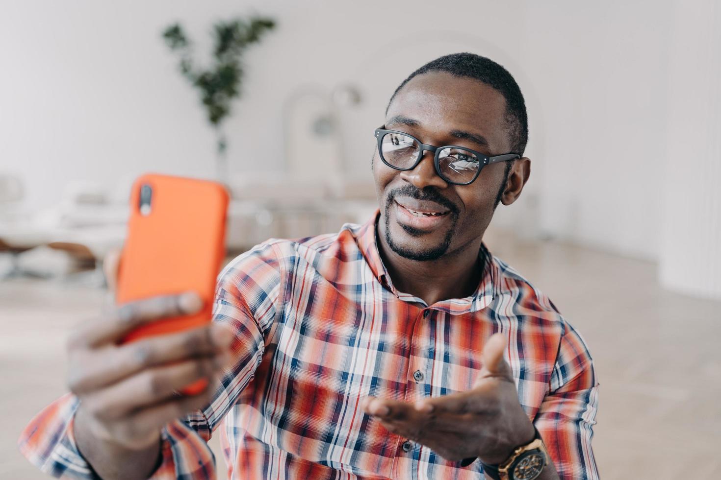 African american man in glasses holding smartphone uses modern apps talking online by video call photo