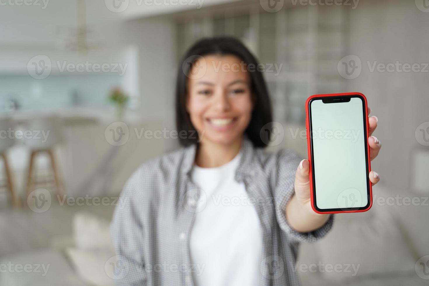 Mobile apps advertisement. Closeup female showing phone with mock up blank screen, standing at home photo