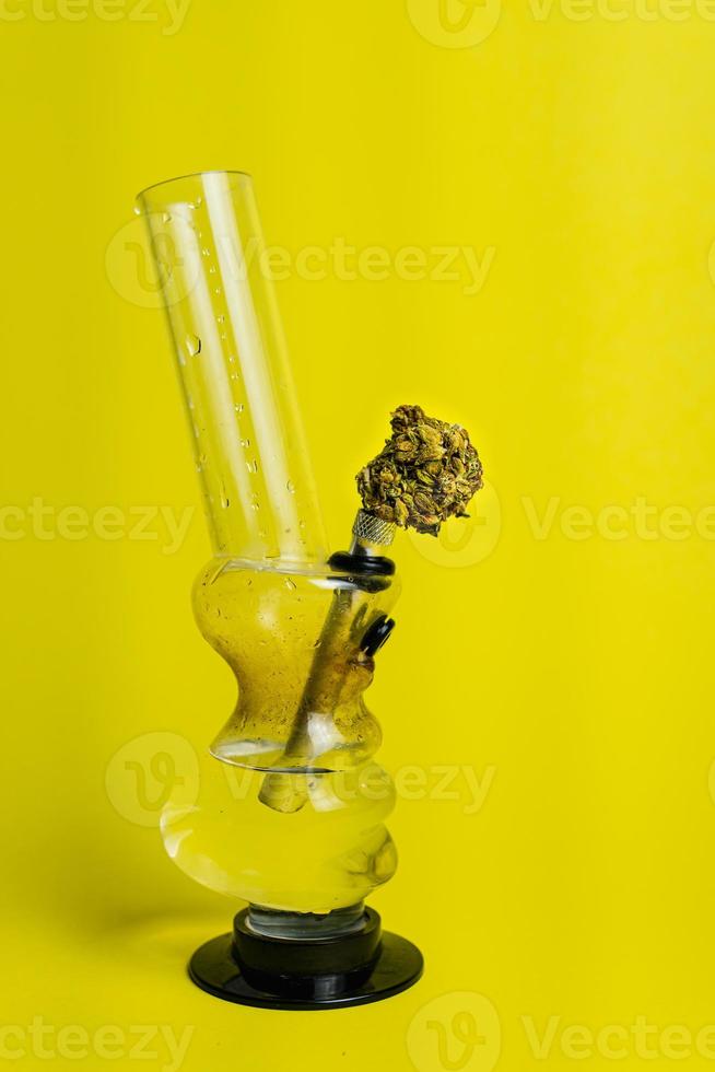 Marijuana bud and bong on yellow background, close up photo