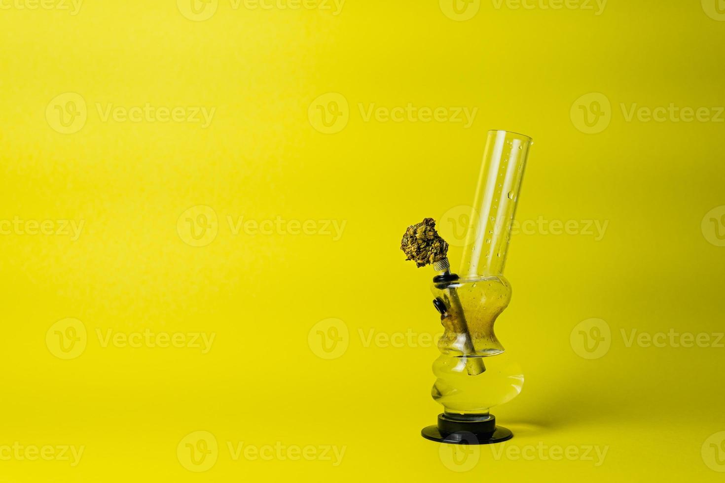 Marijuana bud and bong on yellow background, close up photo