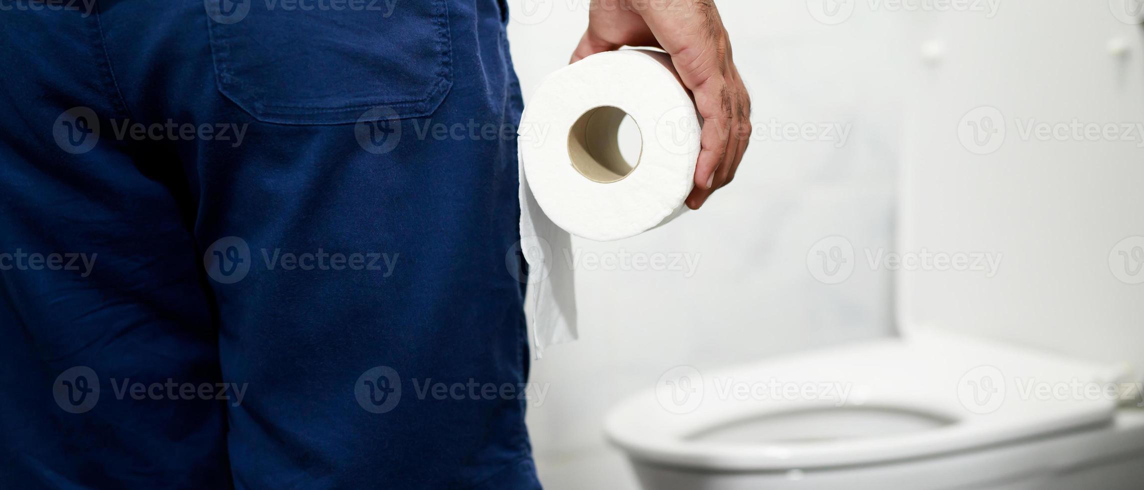 Man suffers from diarrhea hand hold tissue paper roll in front of toilet bowl. constipation in bathroom. Treatment stomach pain and Hygiene, health care photo