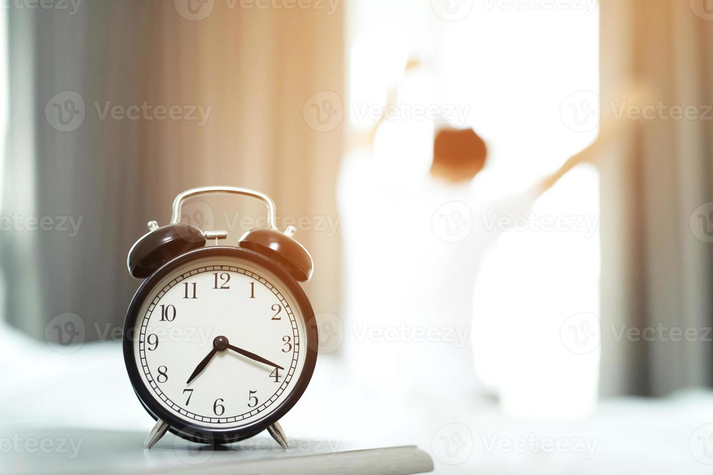 el hombre odia despertarse temprano en la mañana. chica somnolienta mirando el despertador y tratando de esconderse debajo de la almohada foto