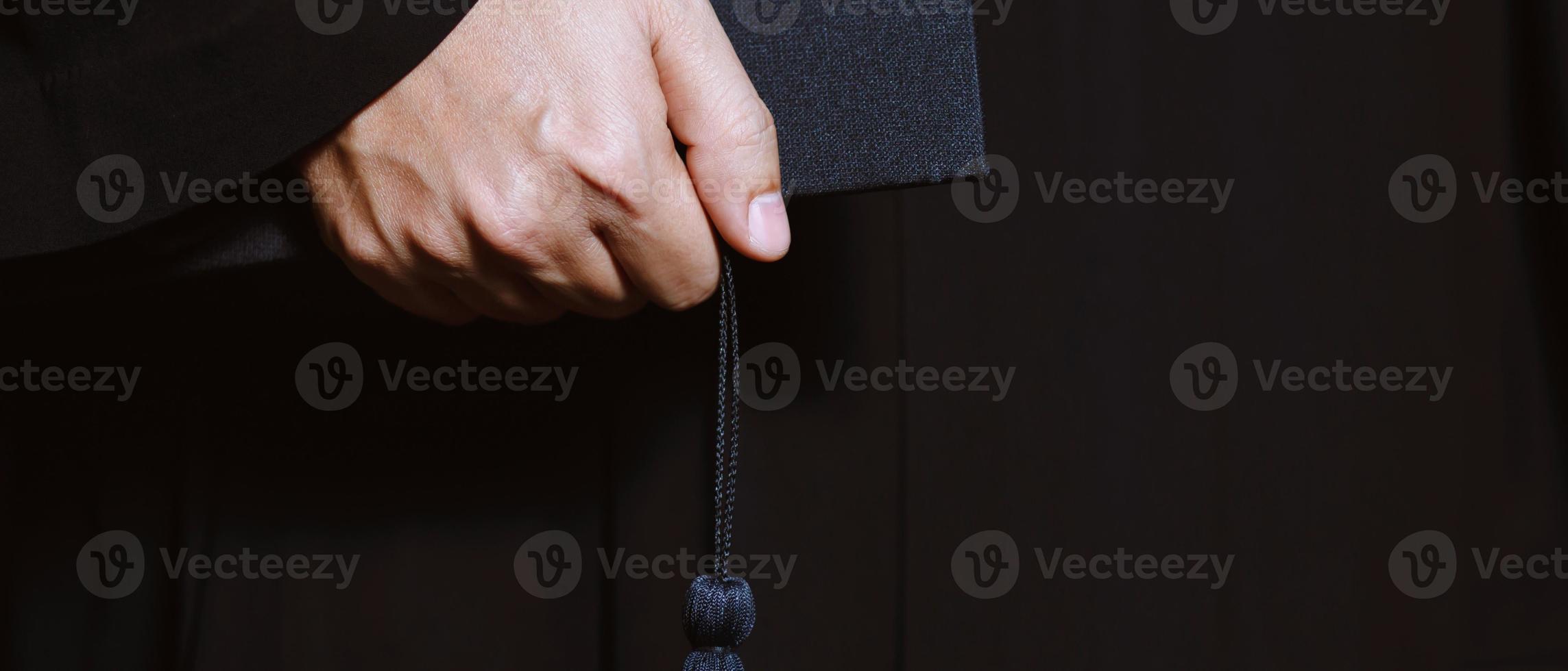 close up graduate hand hold show hat in background school building. Shot of graduation cap during commencement university degree , Education Student Success Learning Concept. photo