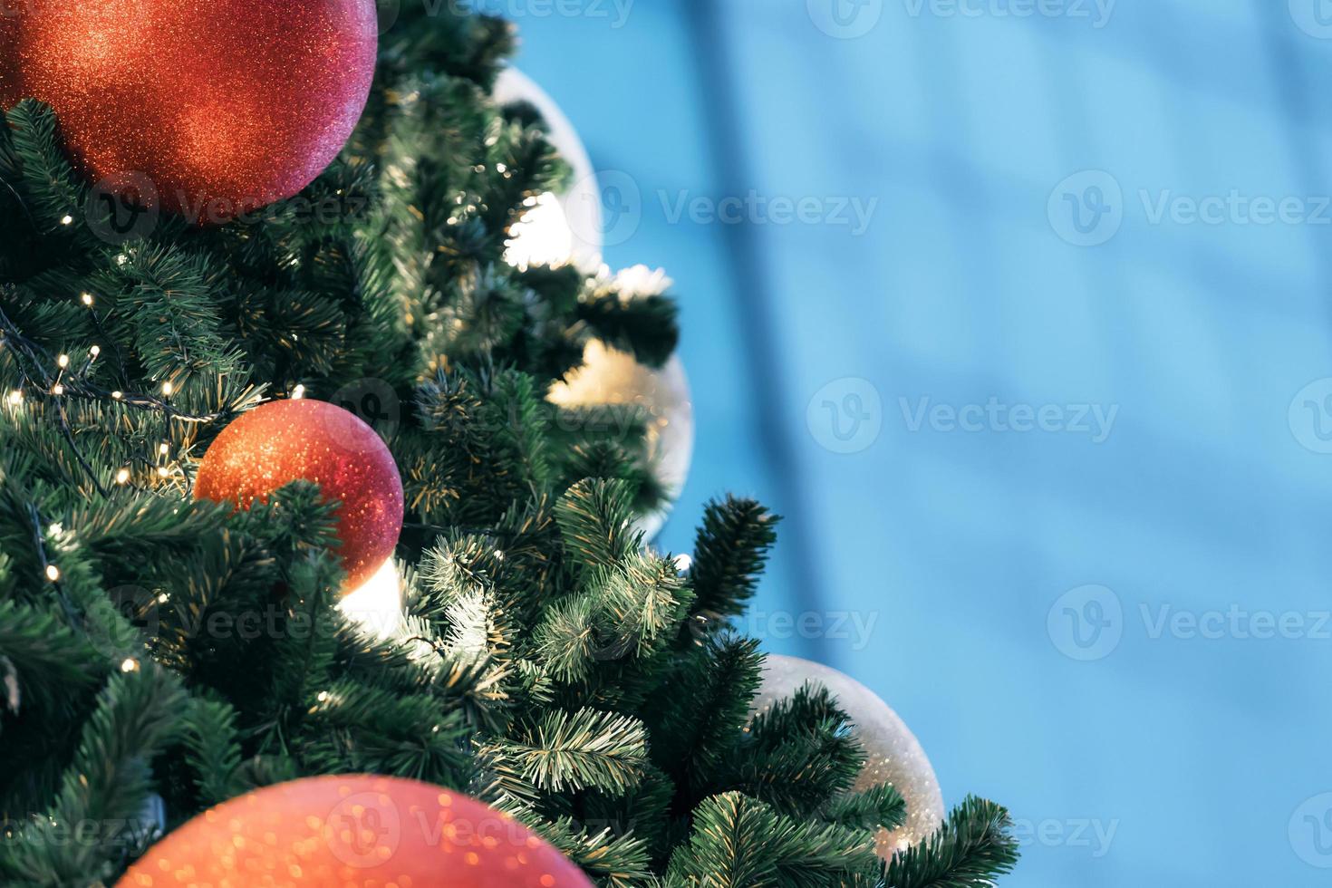 Closeup of red bauble hanging from a decorated christmas tree on blurred of  lights with decorated tree, sparkling and bokeh background. copy space for your text. photo