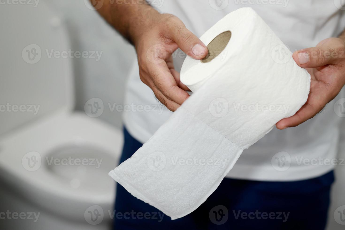 Man suffers from diarrhea hand hold tissue paper roll in front of toilet bowl. constipation in bathroom. Treatment stomach pain and Hygiene, health care photo