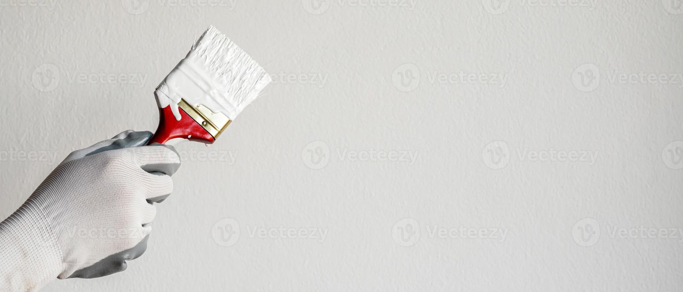 Paint brush, close up hand painter worker painting on surface wall Painting apartment, renovating with white color paint. Leave empty copy space to write descriptive text beside. photo