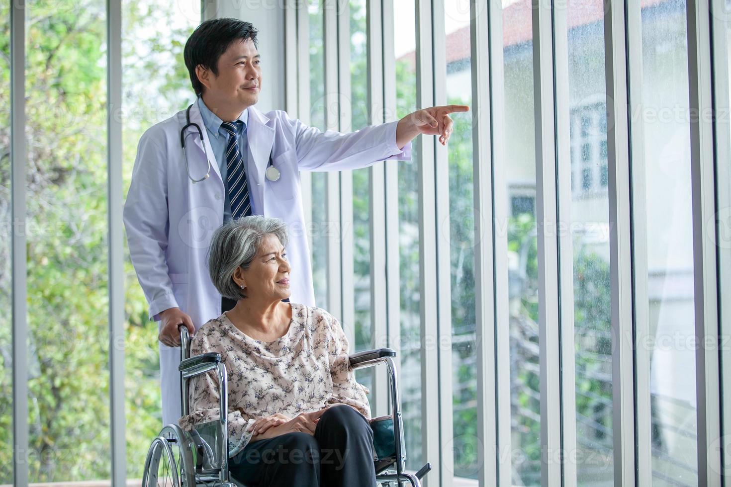 médico asiático apoyando y animando a un paciente mayor en silla de ruedas hablando, sonriendo cómodamente en casa. concepto de salud y medicina. foto