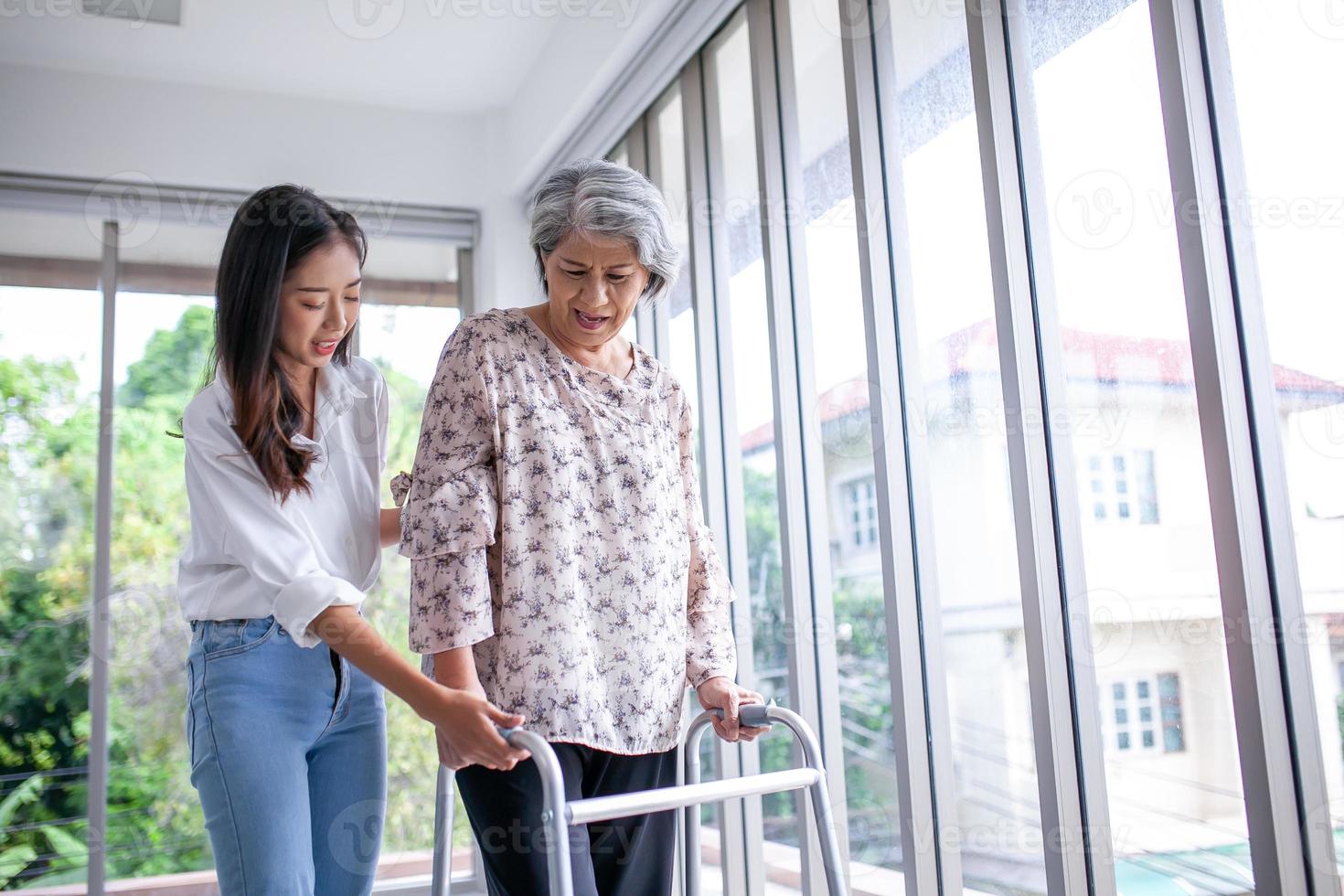 Asian girl assisting elderly woman trying to walk at home, health care. photo