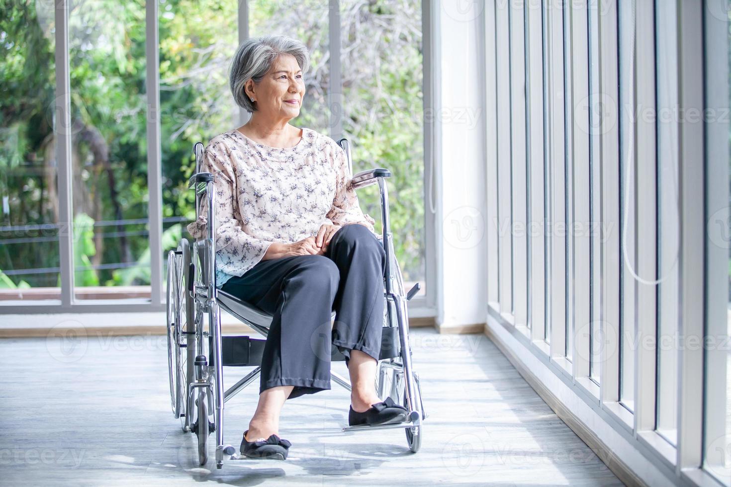 Happy elderly asian woman sitting on wheelchair at home, senior therapy patient at home concept. photo