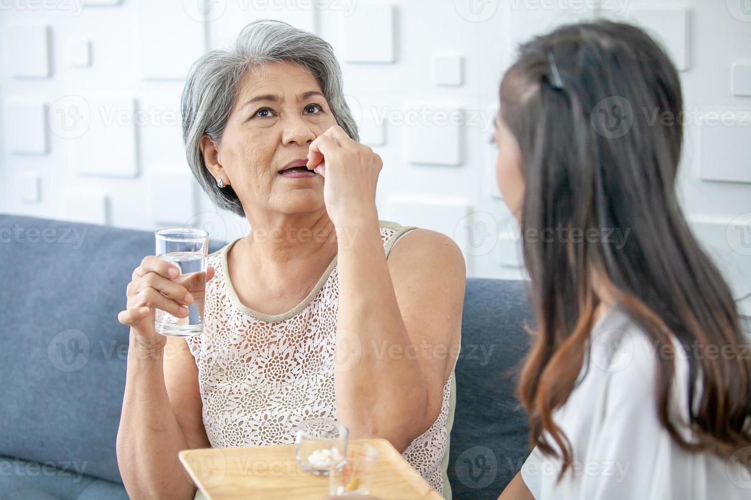 Asian woman, daughter giving daily medicine or vitamin to grandmother at living room in home, Healthcare and medicine concept. photo