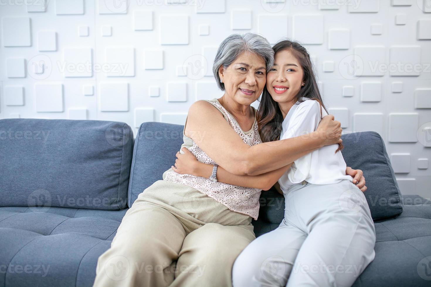 Asian grandma and granddaughter hugged with happy mood on the sofa in home. photo