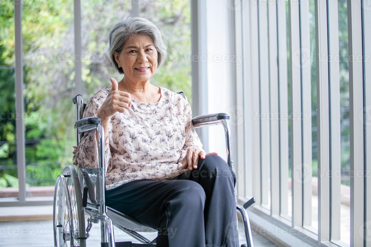 Happy elderly asian woman sitting on wheelchair at home. photo