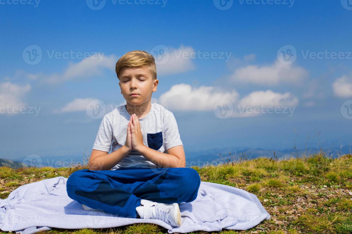 Zen like kid in namaste pose meditating on mountain peak. photo