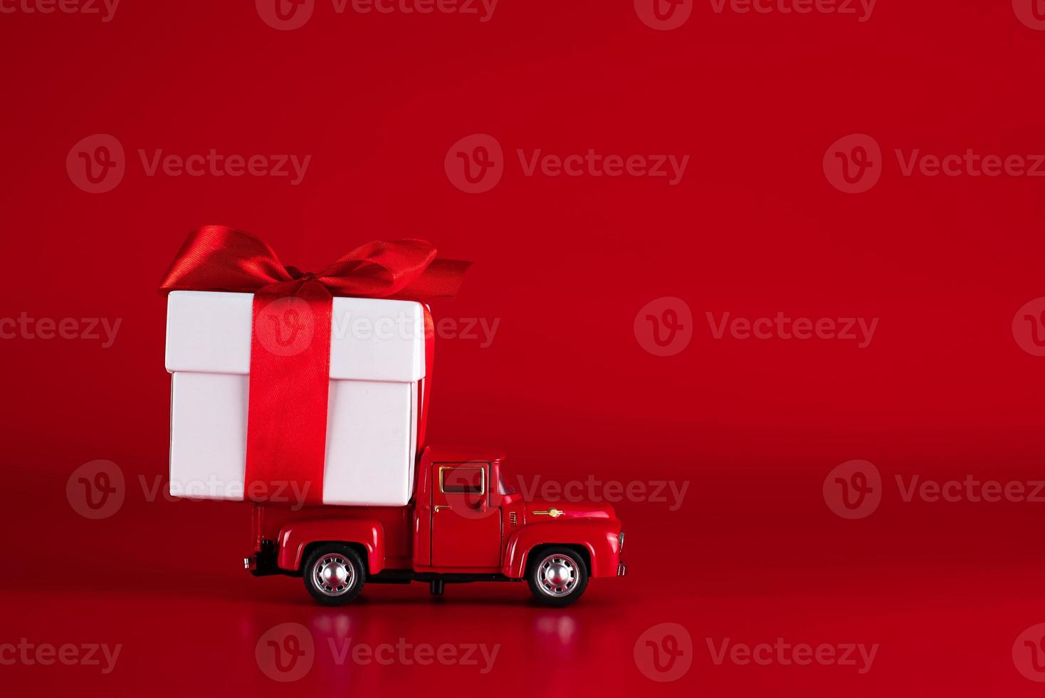 Red car with a gift box on a red background. Concept - delivery of gifts for the holidays, Valentine's Day, International Women's Day, February 14, March 8. Shopping, sale photo